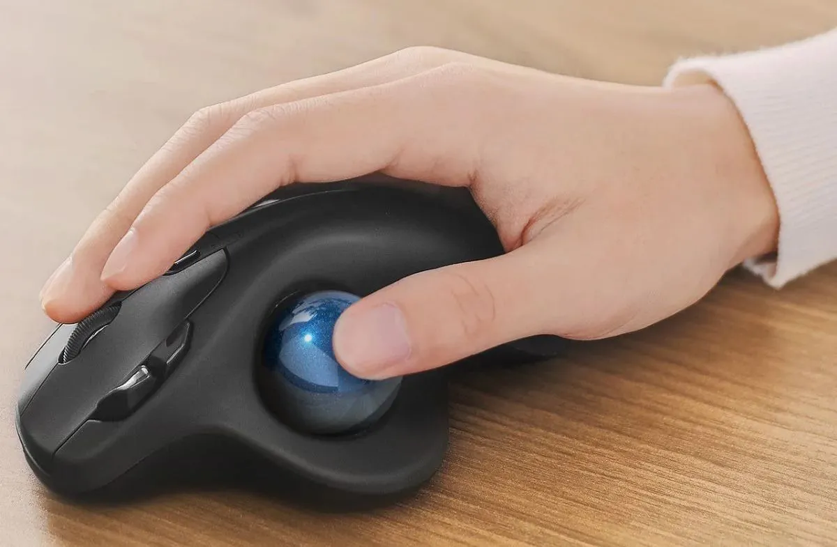 Bàn tay đang sử dụng chuột trackball điều khiển bằng ngón cái, thể hiện tư thế cầm thoải mái.