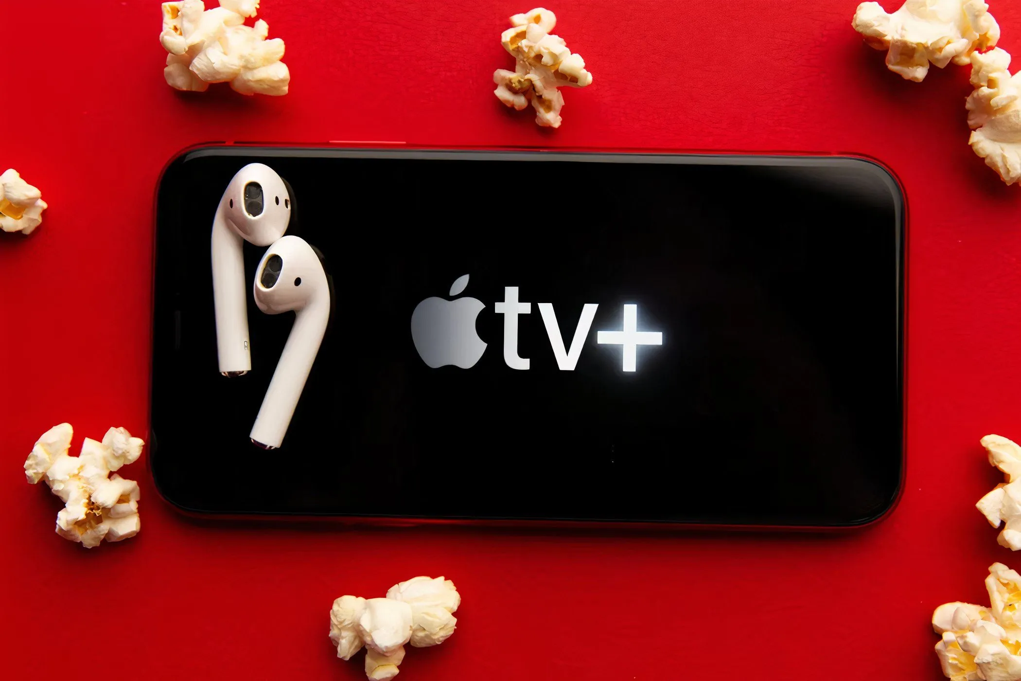 Biểu tượng Apple TV+ trên màn hình điện thoại với bắp rang bơ và tai nghe, thể hiện trải nghiệm xem phim giải trí