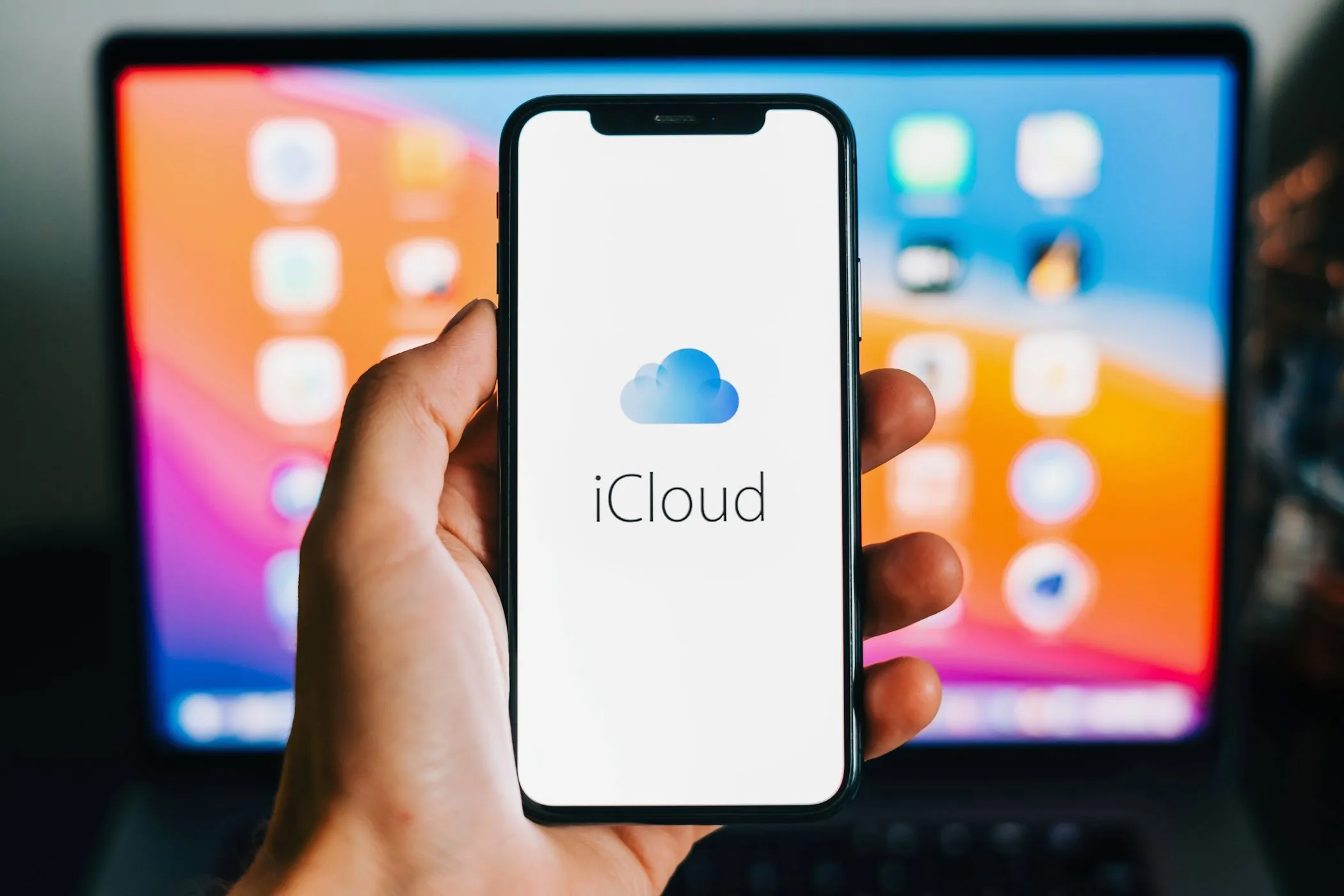 Biểu tượng iCloud hiển thị trên iPhone với MacBook ở hậu cảnh, thể hiện sự tích hợp hệ sinh thái Apple.