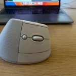 Chuột không dây Logitech Lift màu đen đặt gần máy tính xách tay trên bàn làm việc, thể hiện sự tiện lợi khi làm việc tại nhà