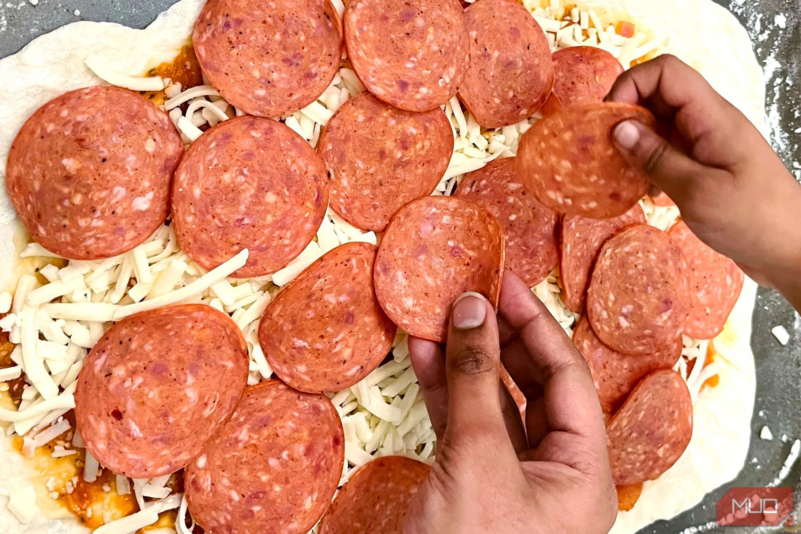 Đôi bàn tay đang rắc phô mai lên bánh pizza, tạo yếu tố con người và kể chuyện cho bức ảnh
