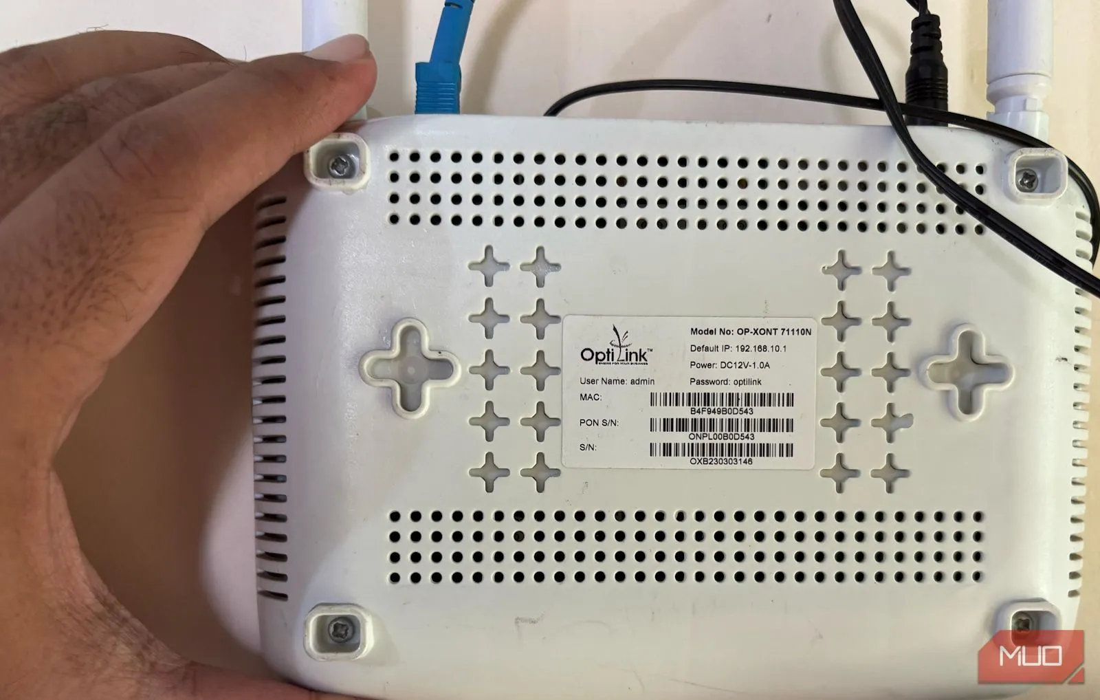 Hình ảnh một bàn tay đang cầm router Wi-Fi và chỉ vào mặt lưng nơi chứa thông tin đăng nhập mặc định.