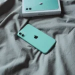 iPhone 11 màu xanh bạc hà đặt trên ga trải giường màu trắng, thể hiện chất lượng hoàn thiện bền bỉ của điện thoại