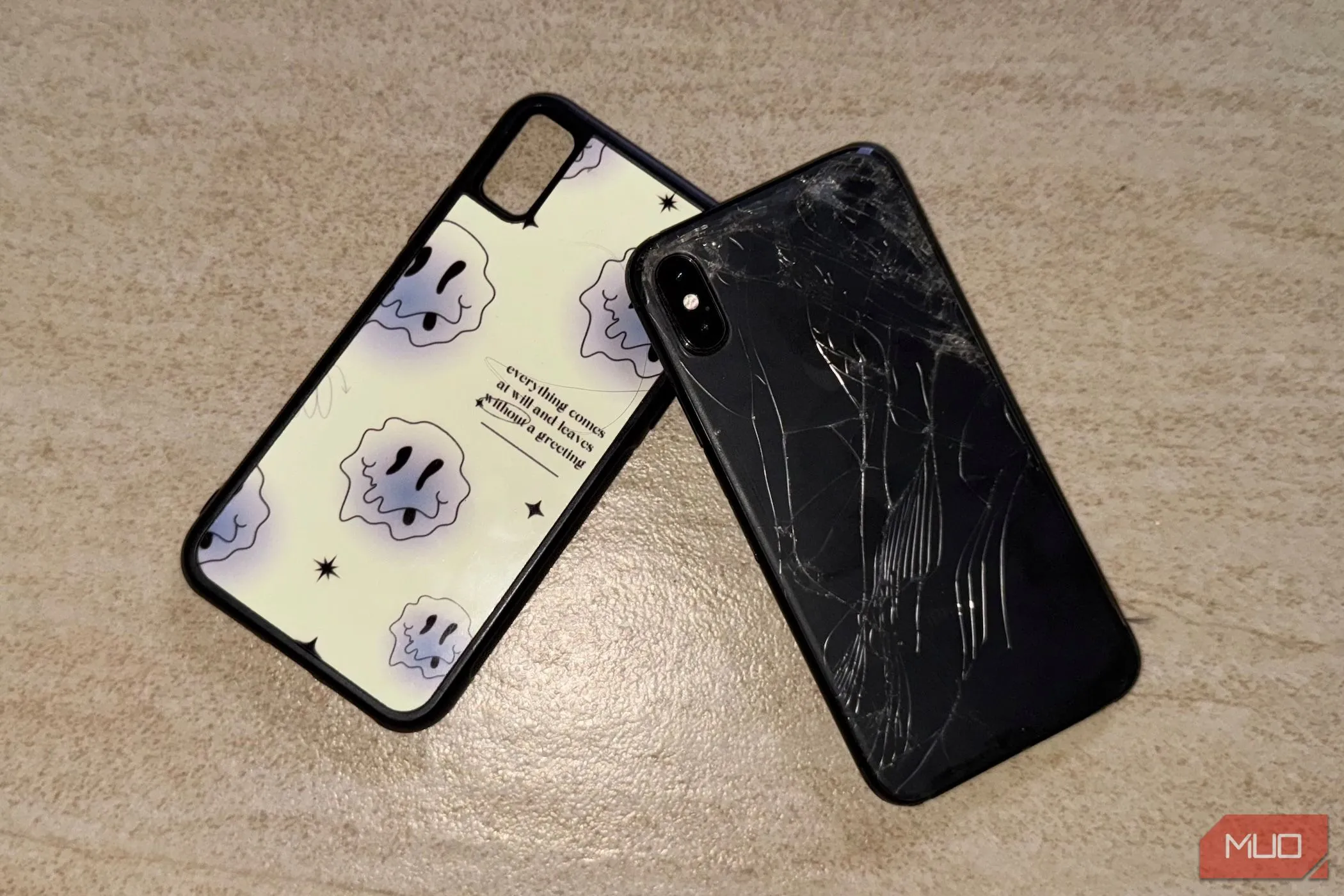 iPhone X với mặt lưng kính bị nứt vỡ, nằm trên sàn cùng ốp lưng, minh họa độ bền kém của vật liệu kính