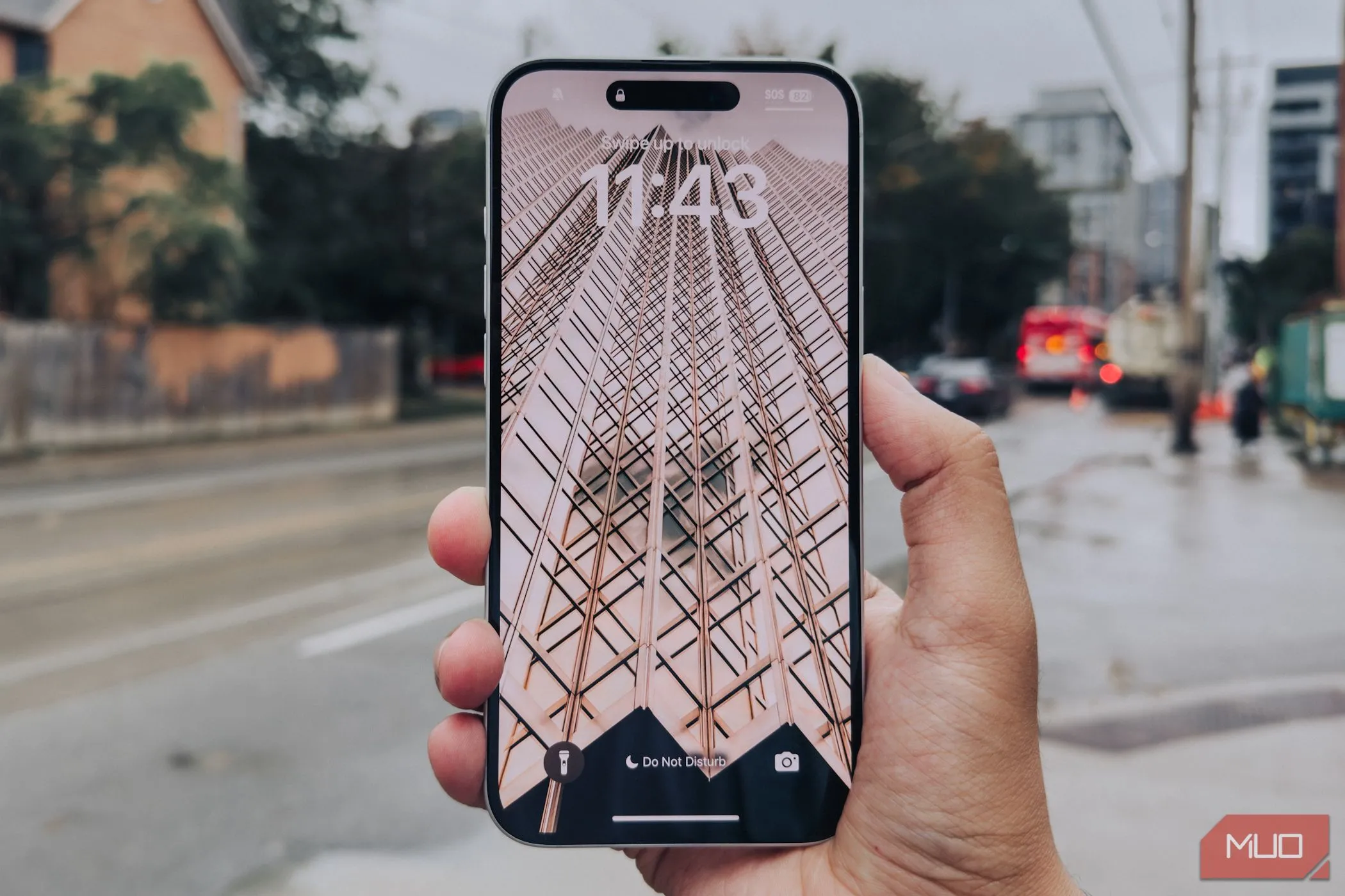 Màn hình iPhone 16 Plus với viền mỏng được cầm trên tay, phía sau là cảnh thành phố, thể hiện xu hướng thiết kế hiện đại