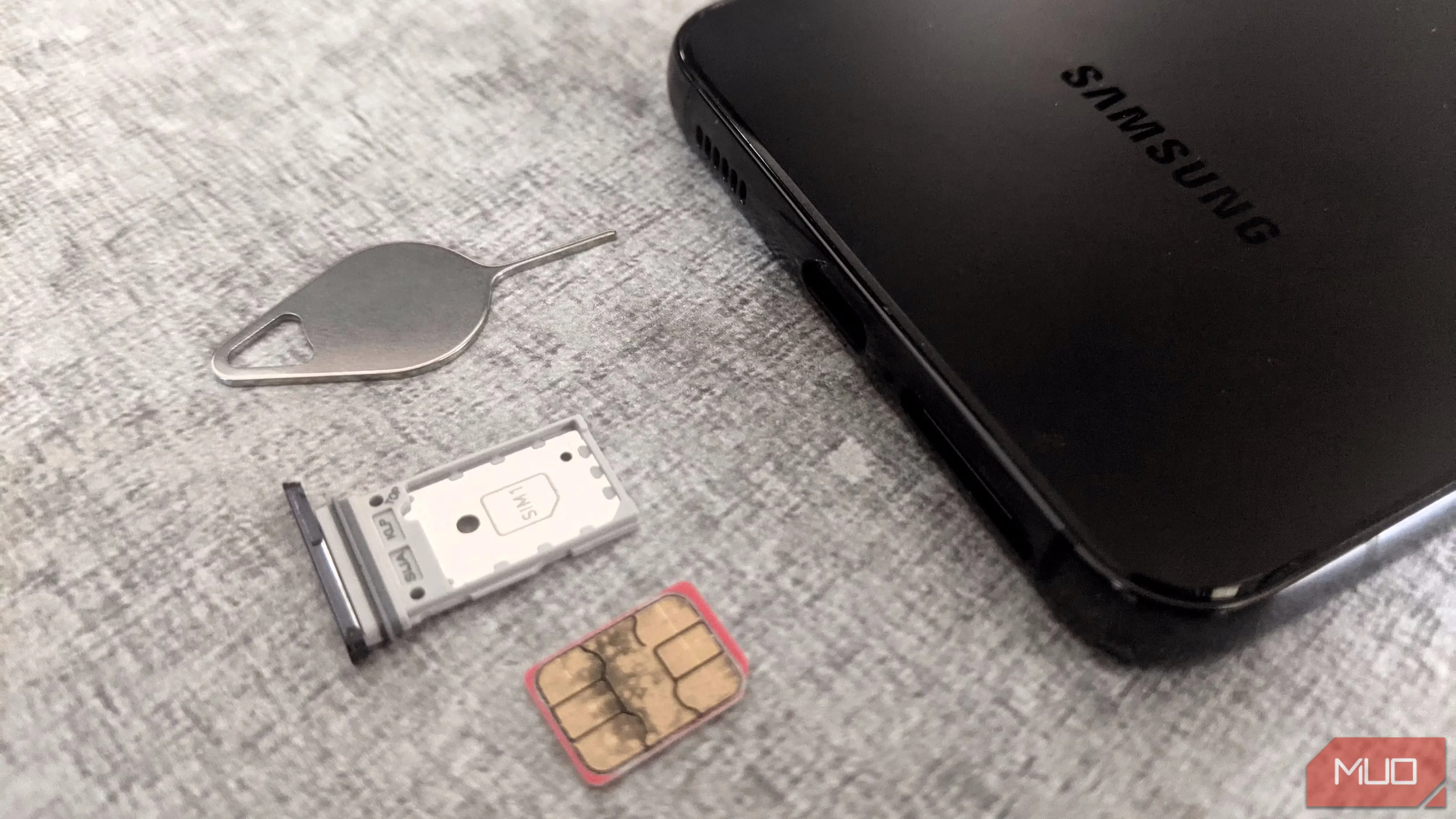 Một điện thoại thông minh Samsung, khay SIM của nó và một công cụ đẩy SIM nằm trên một bề mặt phẳng.