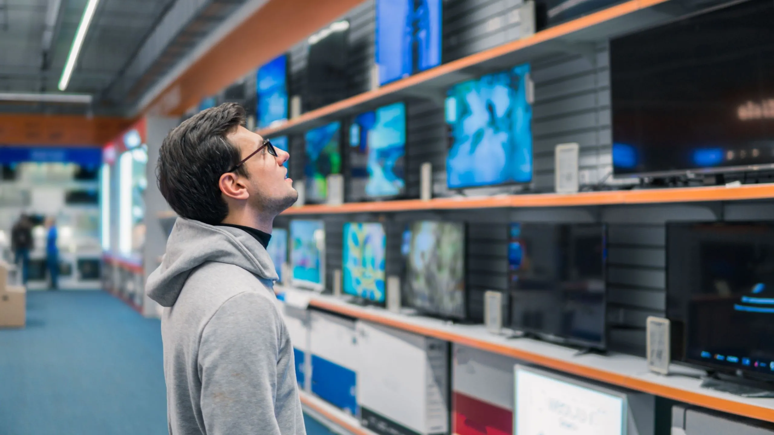 Người đàn ông đang xem xét các mẫu TV thông minh trên kệ hàng trong cửa hàng điện máy