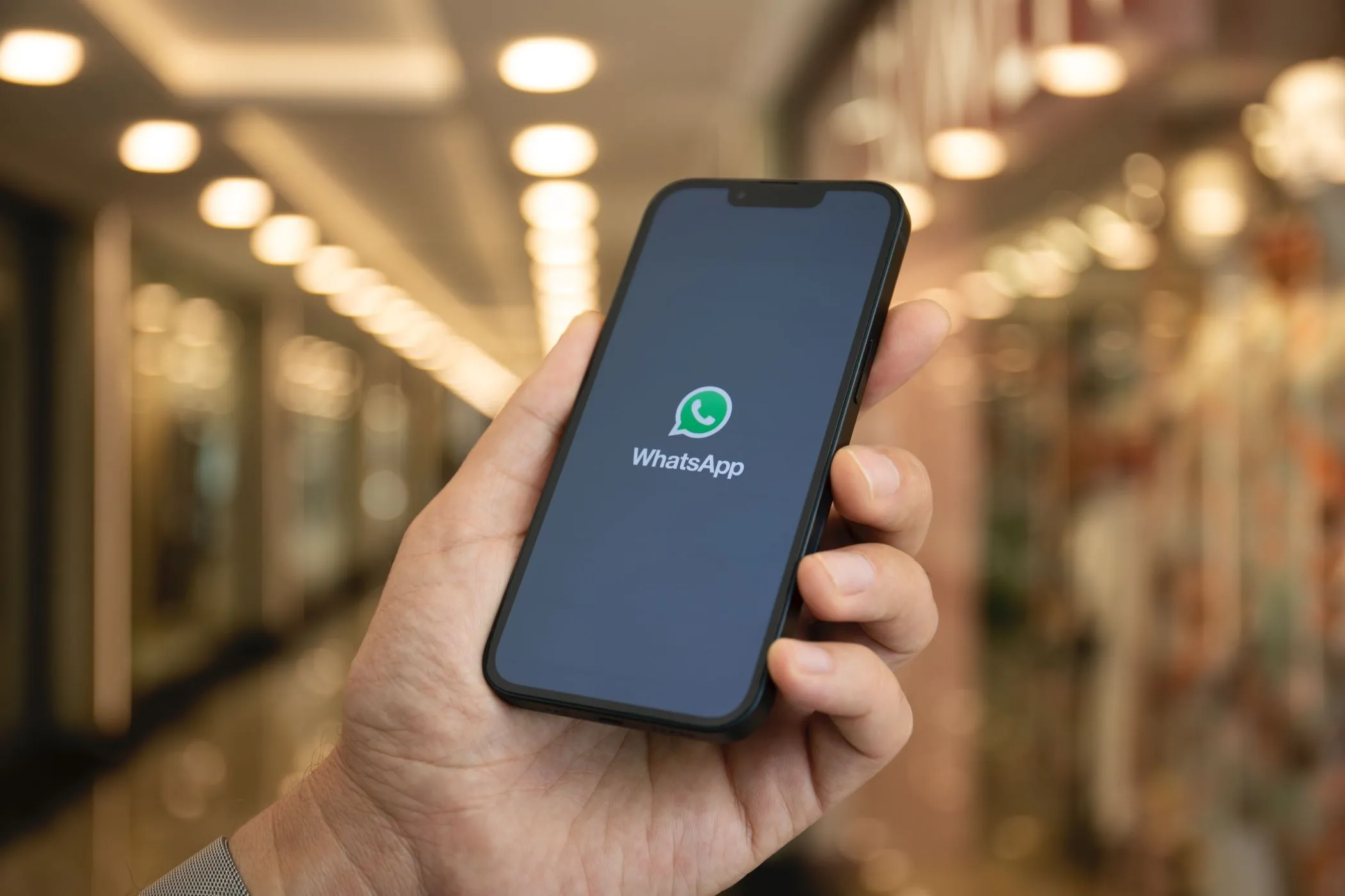 Người dùng cầm điện thoại hiển thị logo WhatsApp, minh họa tính năng chuyển giọng nói thành văn bản