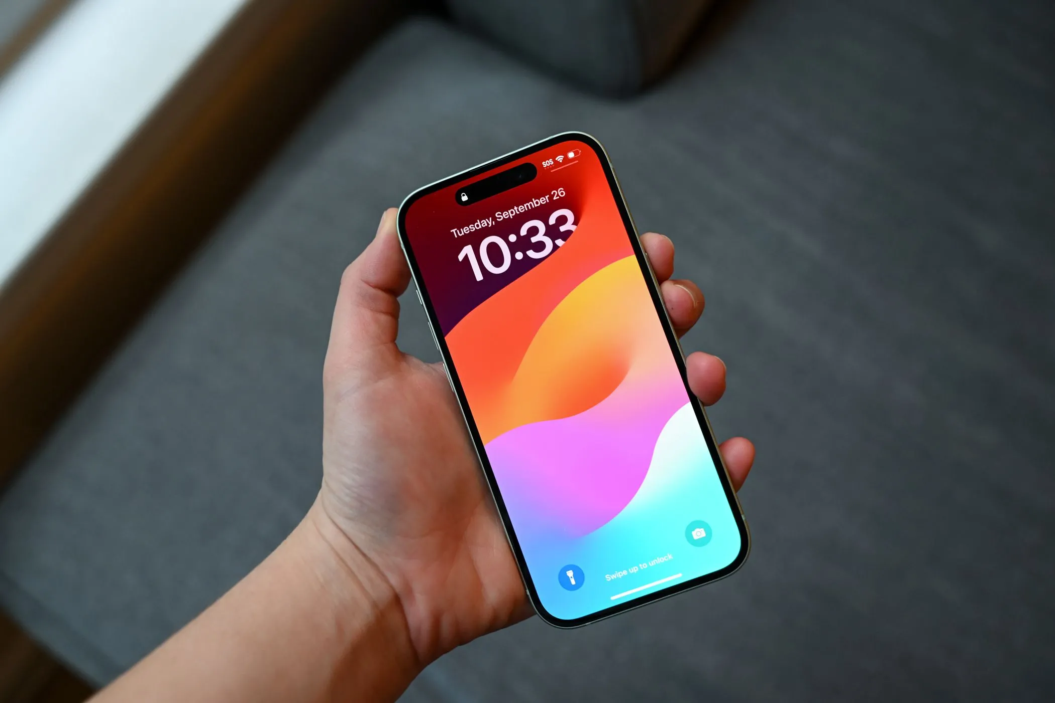 Người dùng đang cầm iPhone 15 hiển thị màn hình khóa, minh họa khả năng che vết xước
