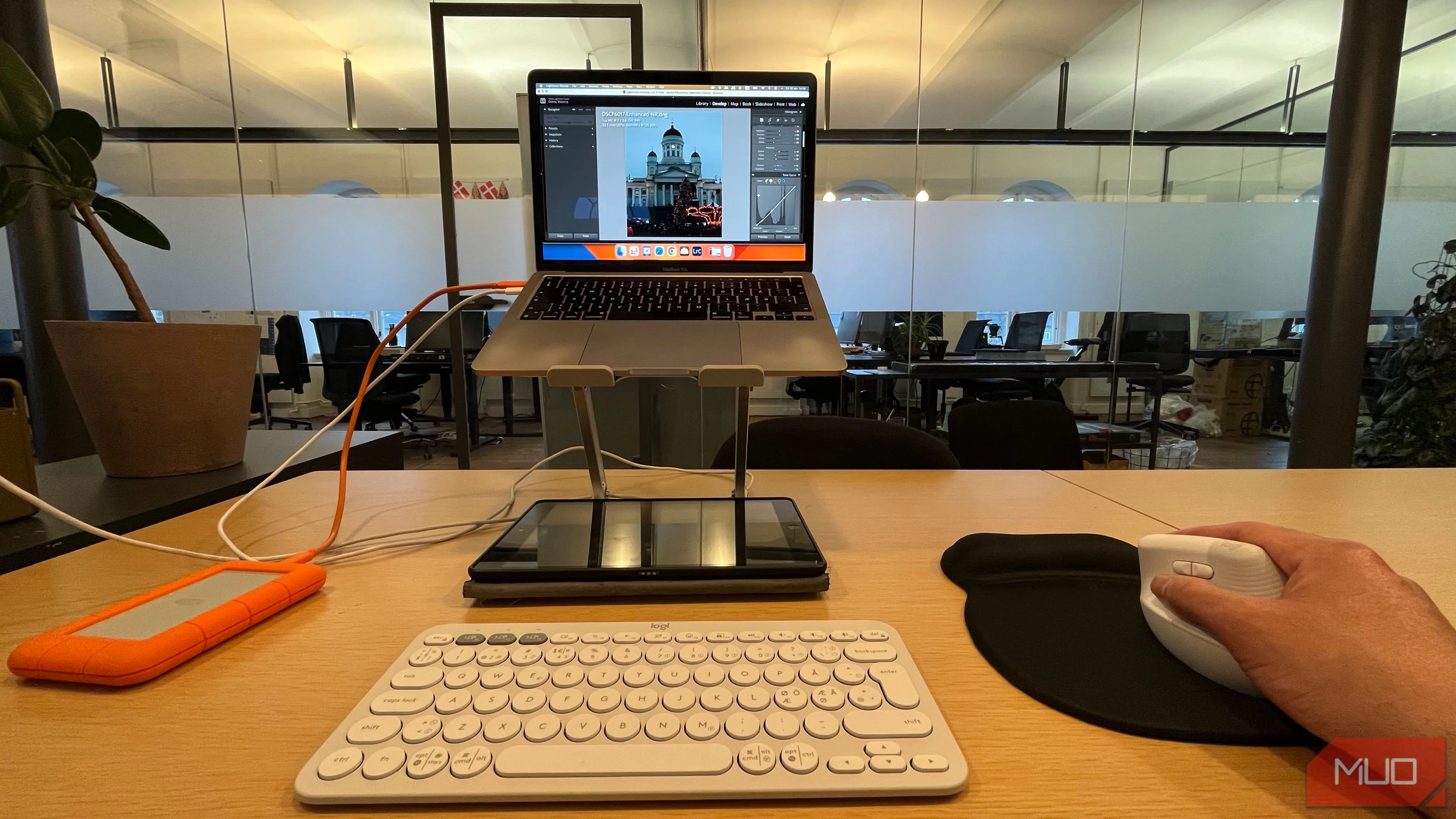 Người dùng đang chỉnh sửa ảnh trên laptop đặt trên giá đỡ, sử dụng chuột không dây, thể hiện tư thế làm việc ergonomic