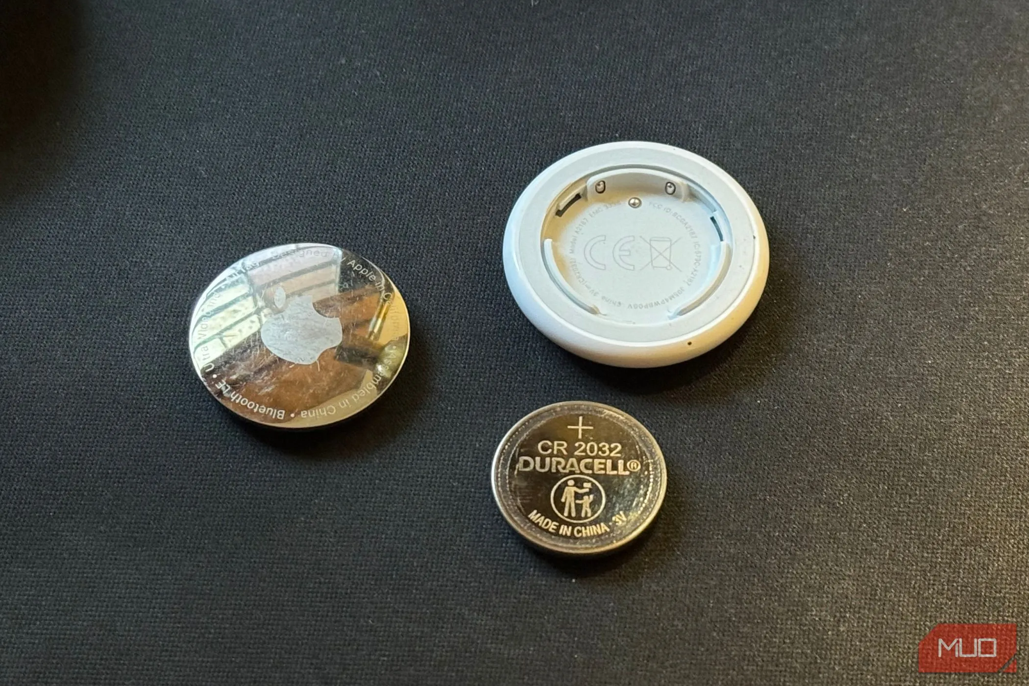 Pin CR2032 và AirTag tháo rời trên nền đen, minh họa việc thay pin AirTag