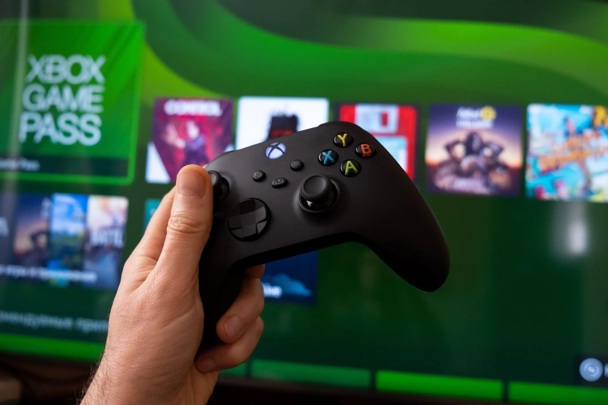 Tay cầm Xbox đặt trên bàn với màn hình chơi game có Game Pass phía sau, minh họa trải nghiệm game với soundbar.