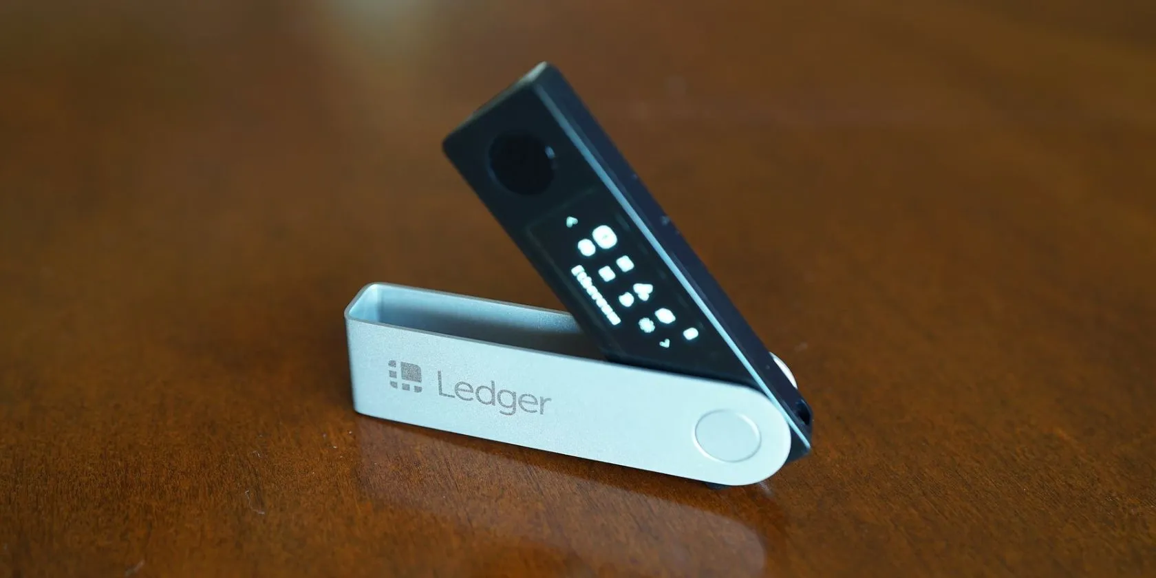 Thiết bị ví lạnh Ledger Nano X màu đen đặt trên bề mặt gỗ.